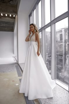 a woman in a white dress is standing by a window and talking on her cell phone