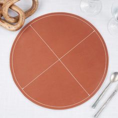 a table setting with utensils, wine glasses and an oval shaped cutting board