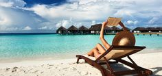 a woman laying in a chair on the beach reading a book