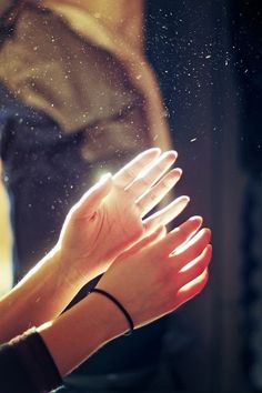 a person holding their hands out in front of a window with rain falling on them