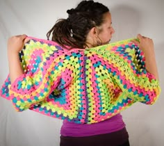 a woman wearing a colorful crochet shawl with her arms around her back