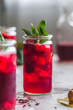 two jars filled with red liquid and mint sprigs next to each other on a table