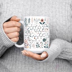 a woman is holding a coffee mug with flowers and leaves on the inside, in front of her