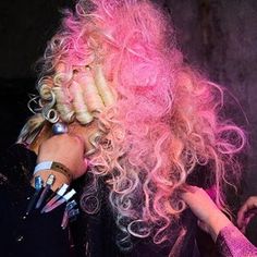 a woman with pink hair is talking on the phone while another person holds her hand up to her ear