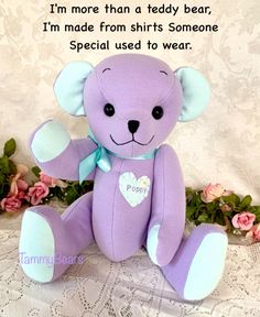 a purple teddy bear sitting on top of a table next to flowers and a lace doily