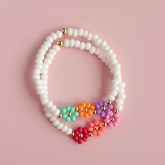 three bracelets with colorful beads on a pink background