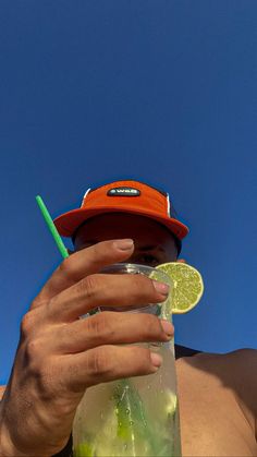 a person holding a drink with a lime slice in it's hand while wearing a red hat