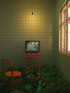 a television sitting on top of a wooden table next to a red chair and window