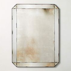 a square mirror mounted on the wall with a white back ground and light brown edges