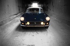 an old black sports car is parked in a dark tunnel with its headlights turned on