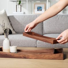 a person placing something in a wooden tray on a table next to a couch and coffee table