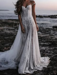 a woman in a wedding dress standing on rocks near the ocean with her hair blowing in the wind