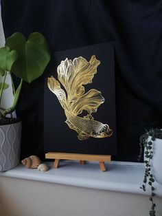 a black and gold painting on a wooden easel next to a potted plant