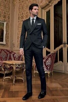 a man in a black suit and tie standing on a hard wood floor next to chairs