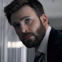 a man with a beard wearing a suit and tie looking at something in the distance