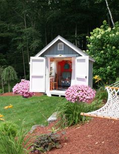 a small white shed sitting in the middle of a lush green field next to flowers