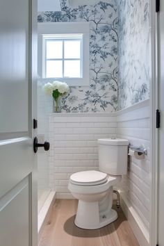 a white toilet sitting inside of a bathroom next to a window with blue and white wallpaper