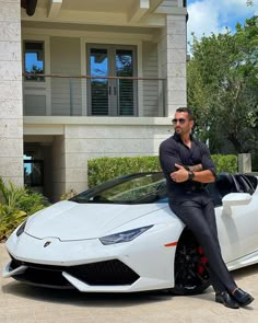 a man sitting on the hood of a white sports car in front of a house