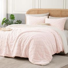 a bed with pink comforter and pillows in a room next to a potted plant