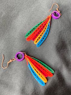 two pairs of multicolored plastic earrings hanging from hooks on a gray cloth background