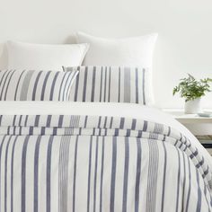 a bed with white and blue striped comforter on top of it next to a table