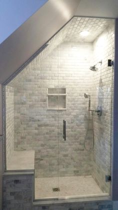 a walk in shower sitting next to a white tiled wall and floor under a slanted ceiling