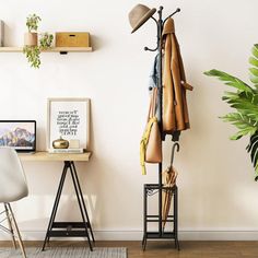 a coat rack with hats and umbrellas on it next to a white chair in front of a potted plant