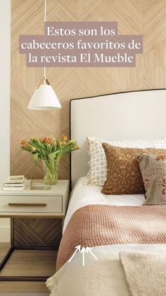 a bed sitting under a lamp next to a white table with flowers on top of it