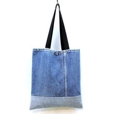 a denim tote bag hanging from a hook on a white wall with black straps