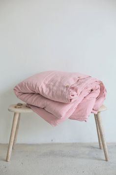 two pink blankets are stacked on top of a wooden bench in front of a white wall