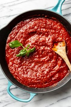 a skillet filled with sauce and a wooden spoon on a marble counter top next to a blue spatula