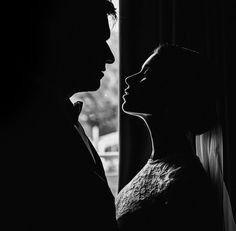 a black and white photo of a man and woman facing each other in front of a window