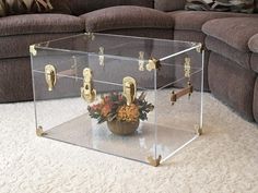 a glass box with flowers in it sitting on the floor next to a brown couch