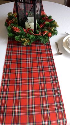 a plaid table runner with a lantern and evergreen wreath on top is ready to be used as a centerpiece