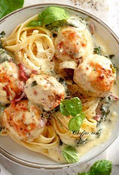 a bowl filled with pasta and meatballs covered in sauce, garnished with fresh basil