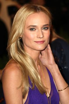 a woman with long blonde hair wearing a purple dress and gold necklace, posing for the camera