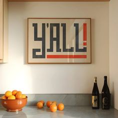 a bowl of oranges sitting on top of a kitchen counter next to bottles of wine