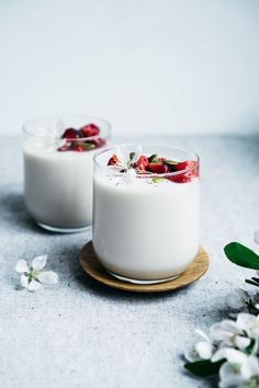 two glasses of yogurt with strawberries on top and flowers in the background