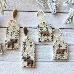 three brown bears are hanging from tags on a white wooden table with pine trees and snow