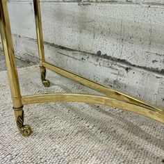 a gold metal and glass console table with wheels on the bottom, in front of a white brick wall