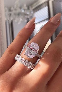 a woman's hand with two engagement rings on her fingers and the ring has an oval shaped diamond surrounded by smaller round diamonds