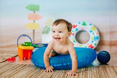 a baby is smiling while sitting on an inflatable raft with toys around him