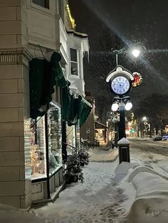 a clock on a pole in the middle of a snow covered street with buildings and lights