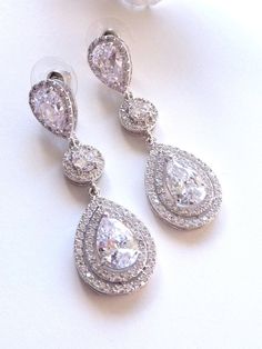 This earring features a white gold plated clear white teardrop cubic zirconia surrounded by 2 layers of little cubic zirconia gems (about 60 gems around it),  dangle from a white gold plated halo round cubic zirconia and a LARGE pear shaped cubic zirconia post earrings. Size: 5.3 (L) x 1.8  (W) cm or 2.1(L)  x 0.72  (W) inches long. Matching Bracelet and Necklace: https://www.etsy.com/listing/225770378/bridal-bracelet-double-halo-round-rose Note: The pear shaped post stud earring used in this design is sightly larger than my other design which has the similar post earrings. If it is a larger pear shaped post stud used, I will mentioned it as large in the listing and the title. **NOTE: CUBIC ZIRCONIA HAS MANY DIFFERENT GRADES, AND ALL THE CUBIC ZIRCONIA USED IN MY DESIGN IS OF THE HIGHEST Q Diamond Teardrop Chandelier Earrings, Diamond White Teardrop Chandelier Earrings With Diamond Accents, Diamond White Teardrop Chandelier Earrings For Anniversary, Dazzling Teardrop Bridal Earrings With Cubic Zirconia, Cubic Zirconia Drop Chandelier Earrings, Pear-shaped Diamond White Cubic Zirconia Bridal Earrings, White Diamond Teardrop Chandelier Earrings, White Teardrop Earrings With Sparkling Stones, White Pear-shaped Cubic Zirconia Diamond Earrings