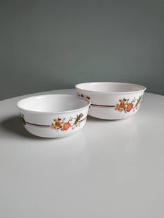 two white bowls sitting on top of a table next to each other and one has an orange flower painted on it