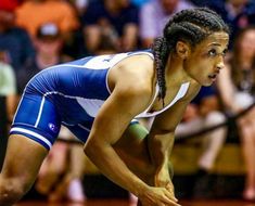 a woman in blue and white wrestling suit crouching down on the ground with her hands behind her head