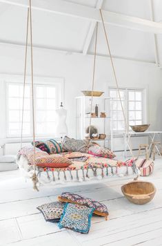 a room with white walls and wooden flooring has a swing bed hanging from the ceiling