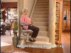 an older woman sitting on a chair in front of a stair case