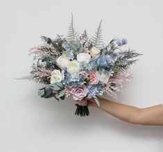 a person holding a bouquet of flowers in their hand on a white background with greenery