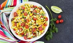 a white bowl filled with corn, tomatoes and cilantro on top of a table